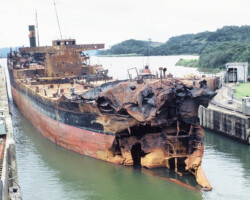 Pan Massachusetts hobbling through the Panama Canal under tow on her way to Kure, Japan to be refitted and placed back in service at the company shipyard. This shows extensive damage from fire following a collision with <em>Phoenix</em> in the Delaware River on 5 June,1953. (From <a href="https://www.czimages.com/CZMemories/Photos/photoof1117.htm"target="_blank" rel="noopener noreferrer">Canal Zone Images</a>)